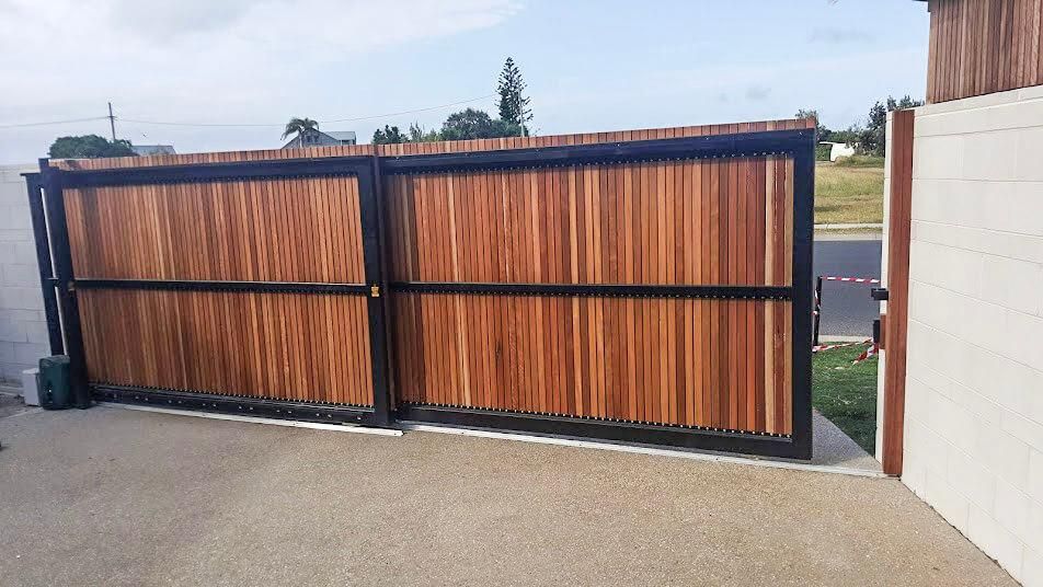 A Wooden Gate with A Black Frame Is Open to A Driveway — Byron & Beyond Fencing In Billinudgel, NSW