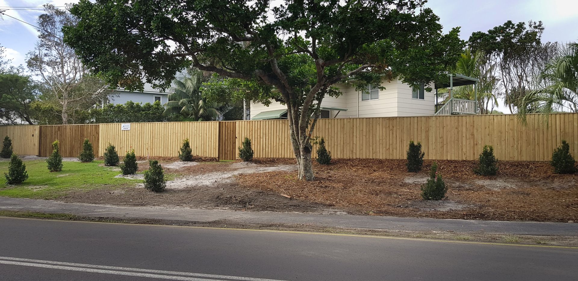 A large timber fence in front of a lawn and house behind it — Byron & Beyond Fencing In Billinudgel, NSW