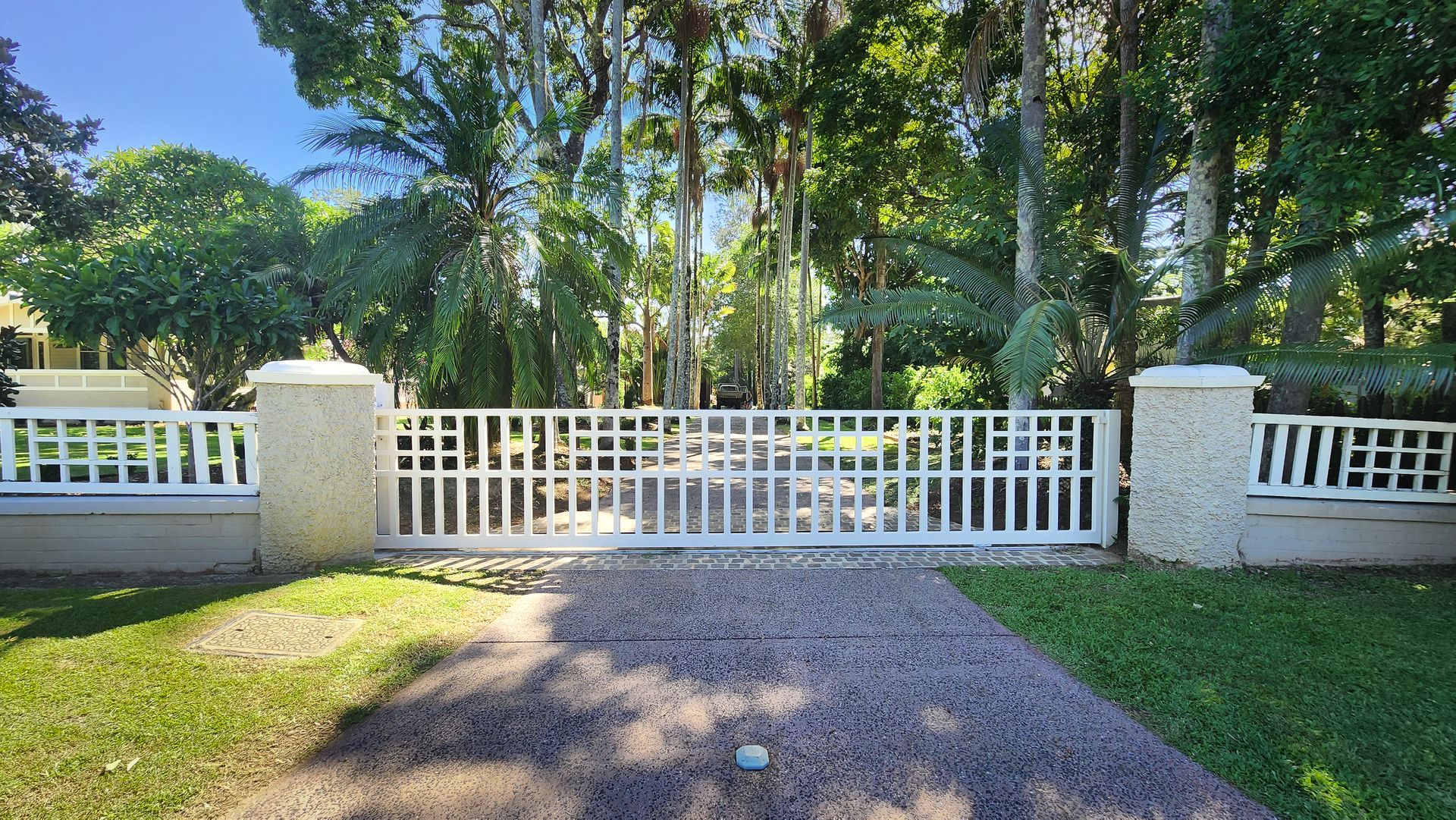 A large white aluminum gate in front of a large set of trees and a drive way — Byron & Beyond Fencing In Billinudgel, NSW