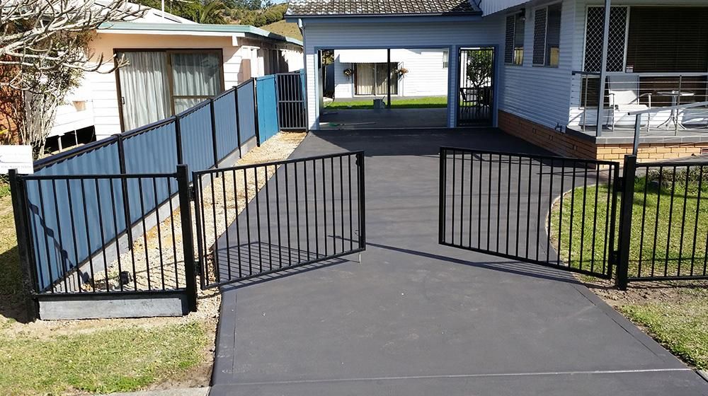A Driveway Leading to A House with A Blue Fence and A Black Swinging Gate — Byron & Beyond Fencing In Billinudgel, NSW 