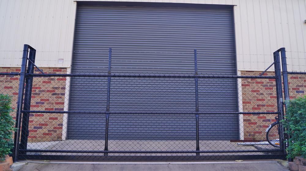 A Black Garage Door Is Behind a Chain Link Fence — Byron & Beyond Fencing In Billinudgel, NSW
