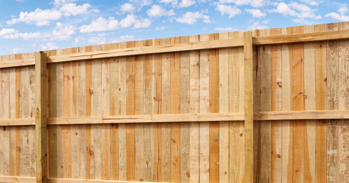 Wooden privacy fence against a blue sky with clouds.