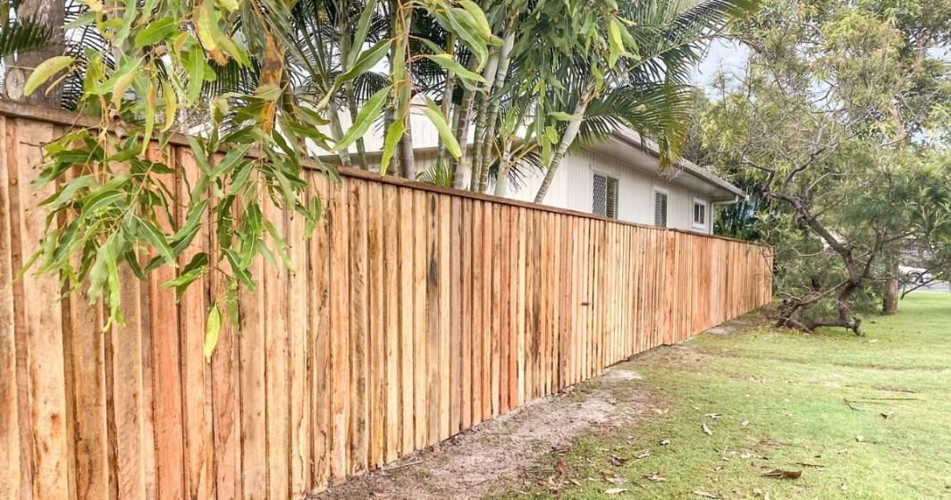 Wooden fence in front of a house, along green grass.