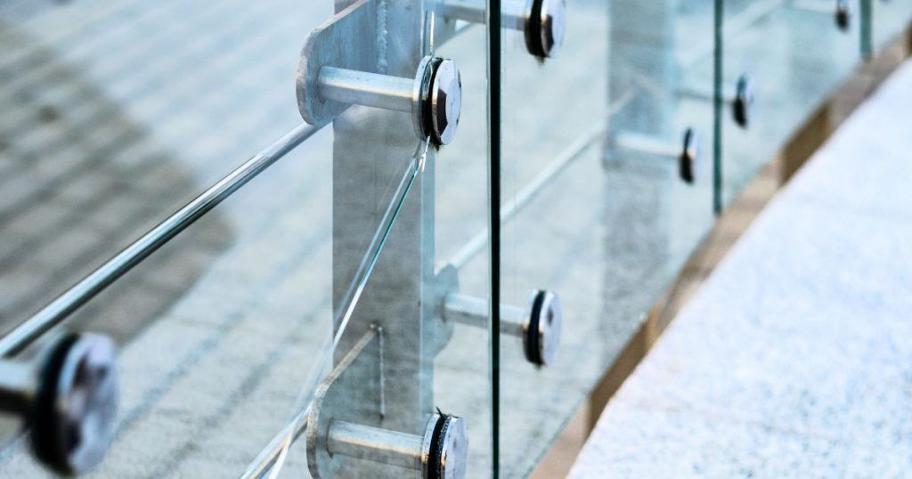 Glass railing with silver posts and horizontal bars, outdoors.