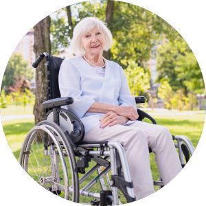 An elderly woman is sitting in a wheelchair in a park.