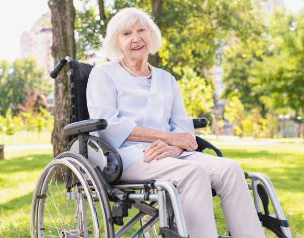 An elderly woman is sitting in a wheelchair in a park.
