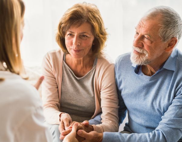 An elderly couple is holding hands while talking to a doctor.