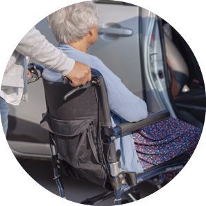 A woman in a wheelchair is being pushed into a car.