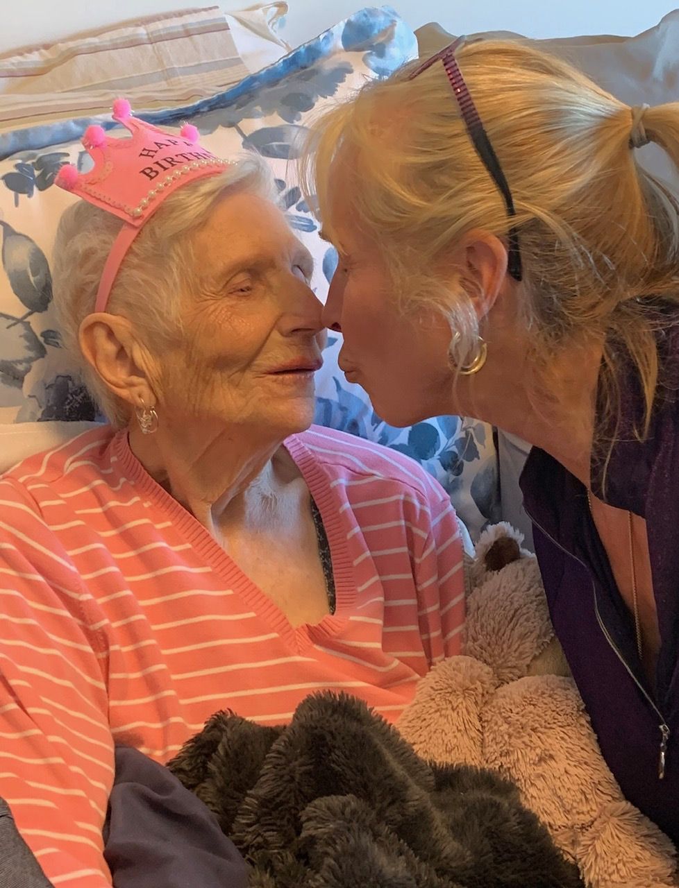 A woman wearing a pink tiara kisses an older woman on the cheek