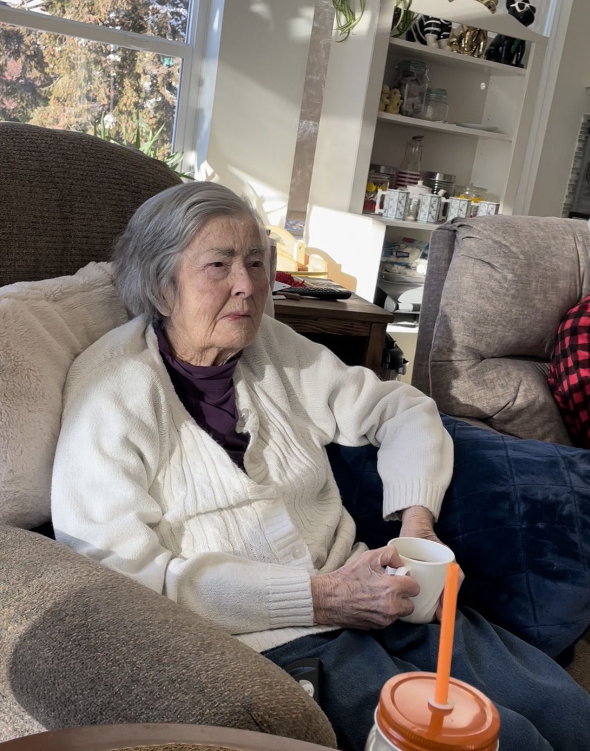 An elderly woman is sitting in a chair holding a cup of coffee