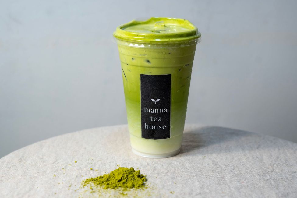 Green takeaway drink cup with lid on a white table, with spilled matcha powder in front
