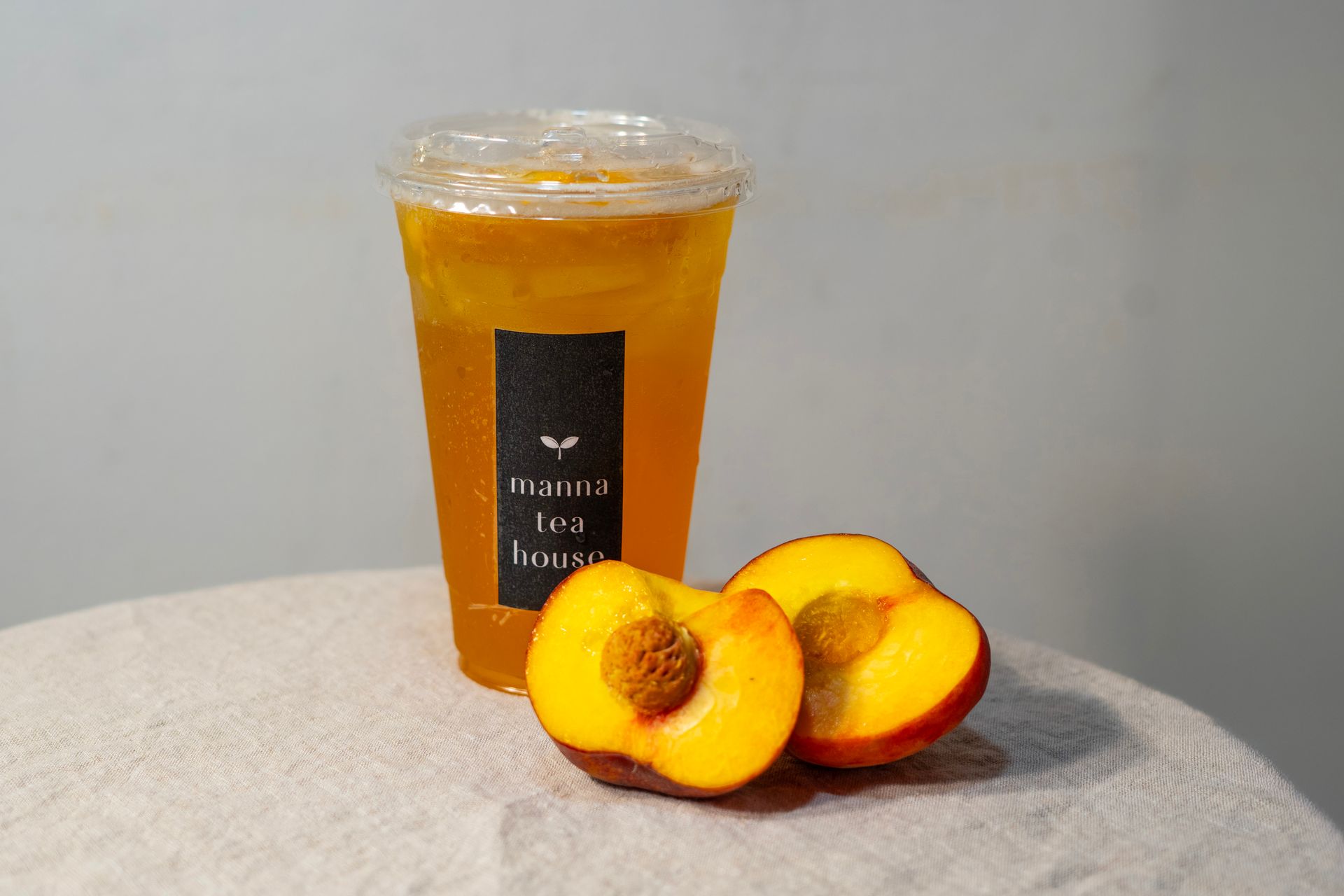 Peach iced drink in a clear cup beside sliced peaches on a gray surface