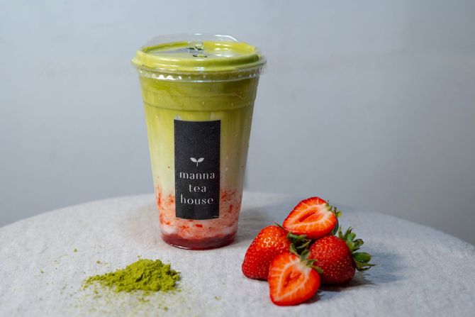 Green strawberry smoothie in a cup with sliced strawberries and matcha powder on a table