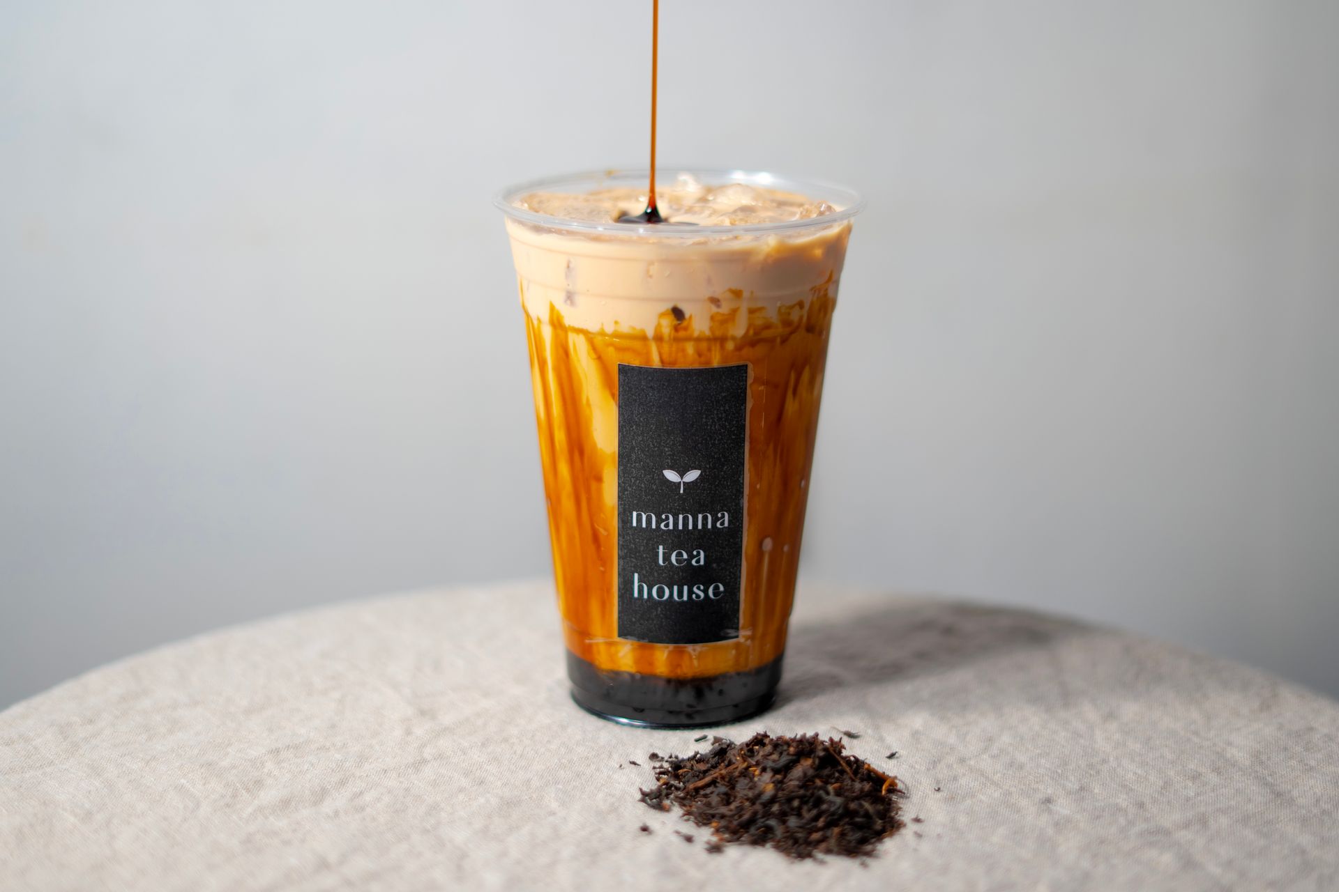 Iced coffee in a clear glass with a straw and spilled grounds on a light tabletop.
