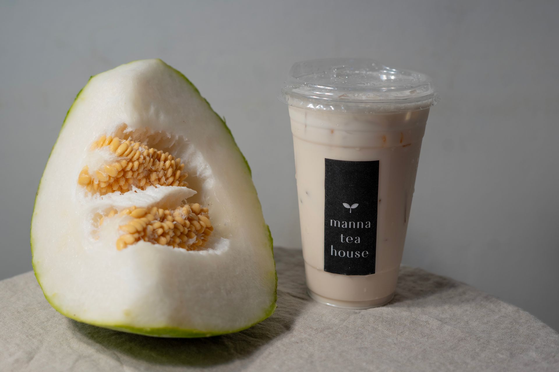 A white-and-green melon half beside a clear iced drink in a plastic cup with a black label.