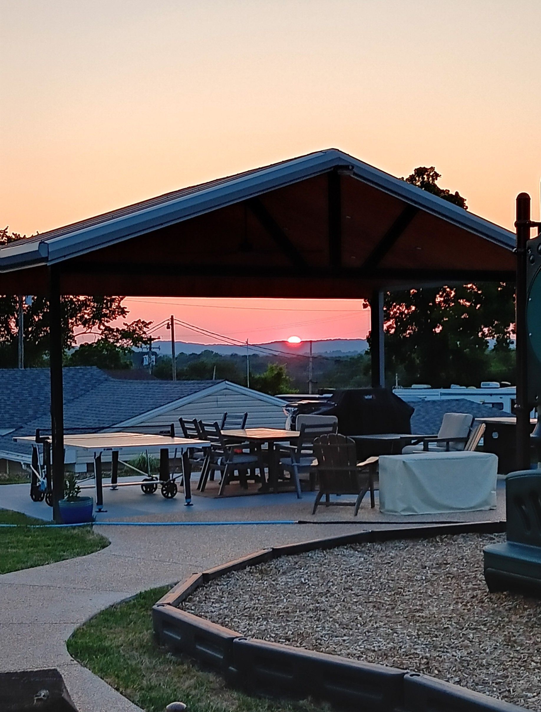 Outdoor patio at sunset with tables, chairs, and a covered pavilion overlooking a distant view.