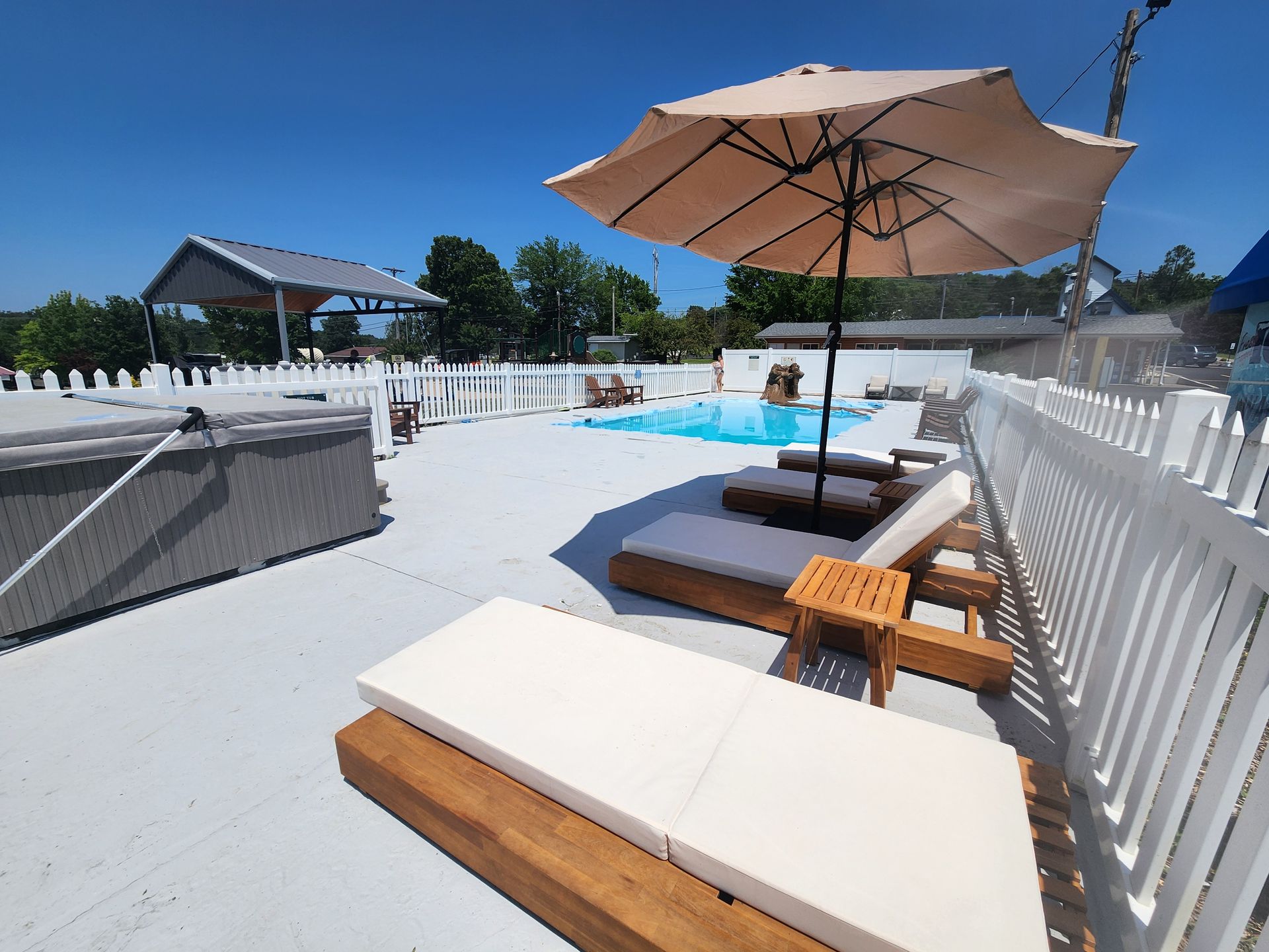 Poolside lounge chairs and umbrella on a sunny patio with white fencing and a blue pool