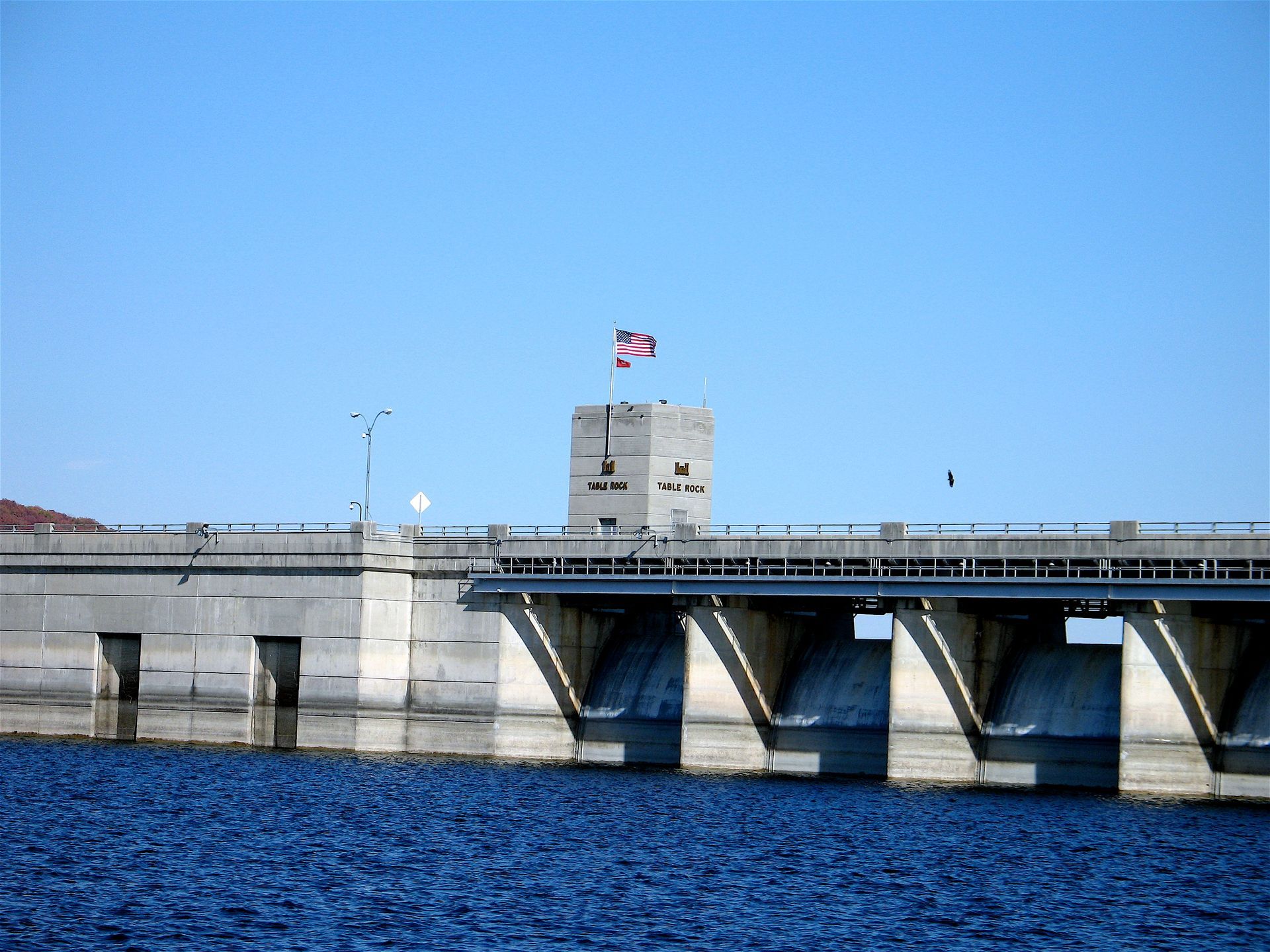 A concrete dam with a Union Jack flag over blue water under a clear sky