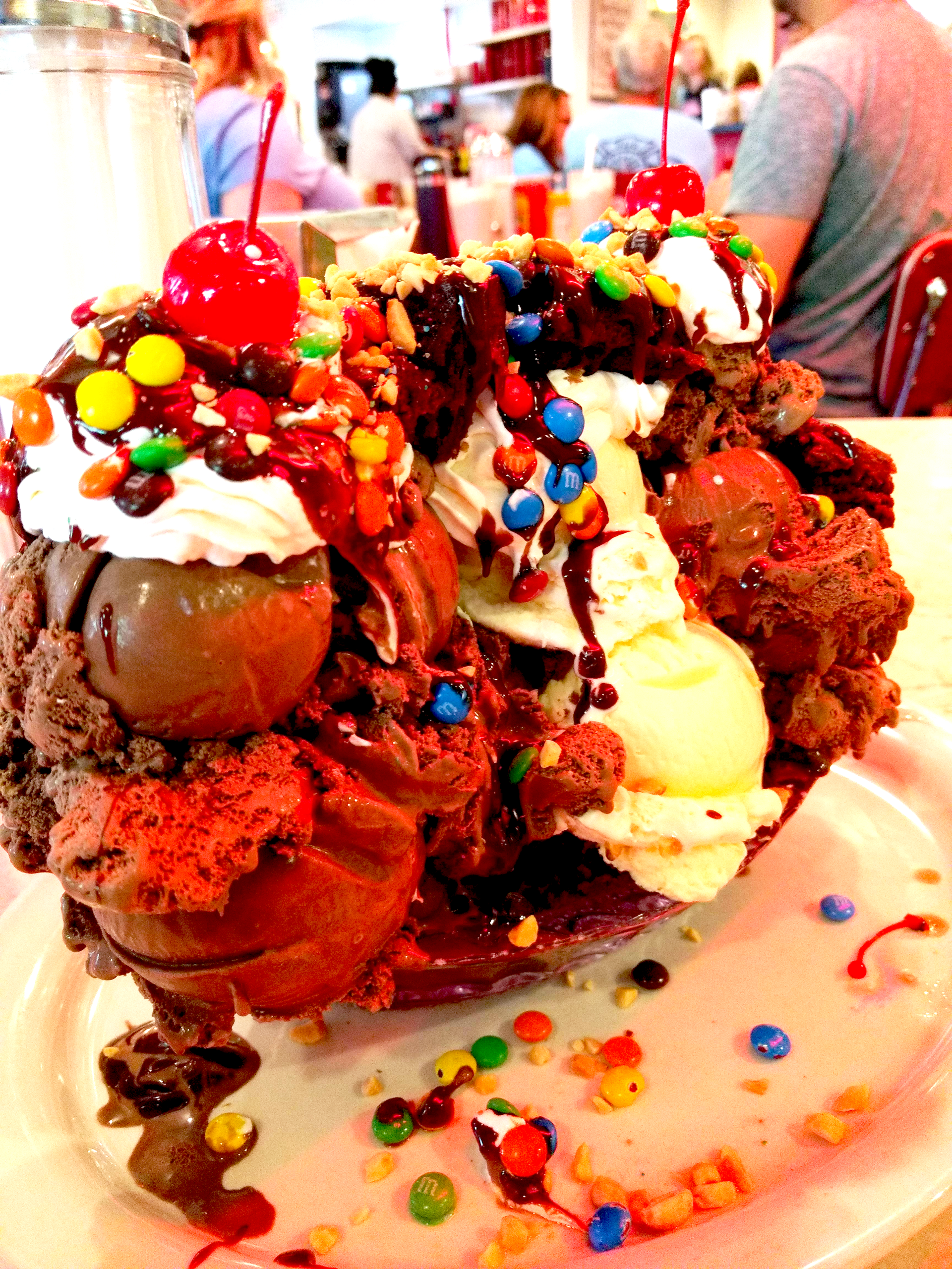 Assorted ice cream sundaes piled high with whipped cream, cherries, chocolate, and colorful candy in a dessert shop.