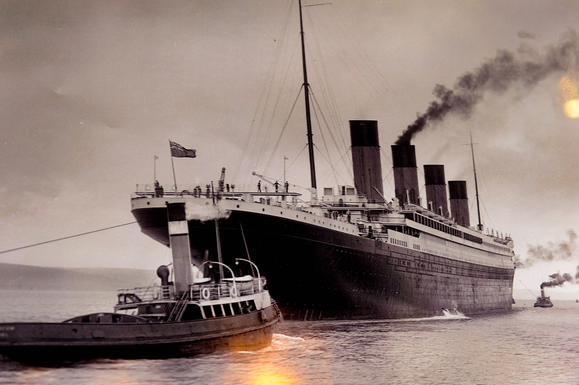 Titanic docked with a tugboat beside it, smoke rising from the ship’s funnels at sea.