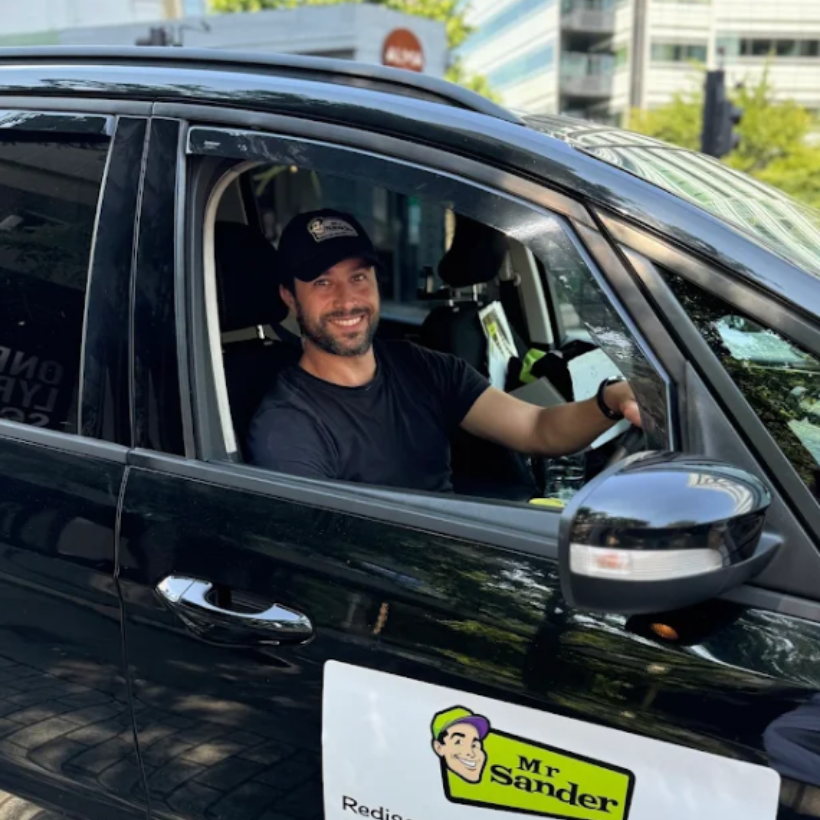 Man in a black car, smiling and looking out window. Sign reads 