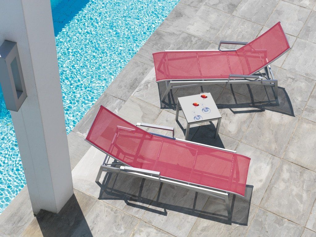 Arredamento da esterno composto da due sdraio e un tavolino a bordo di una piscina.