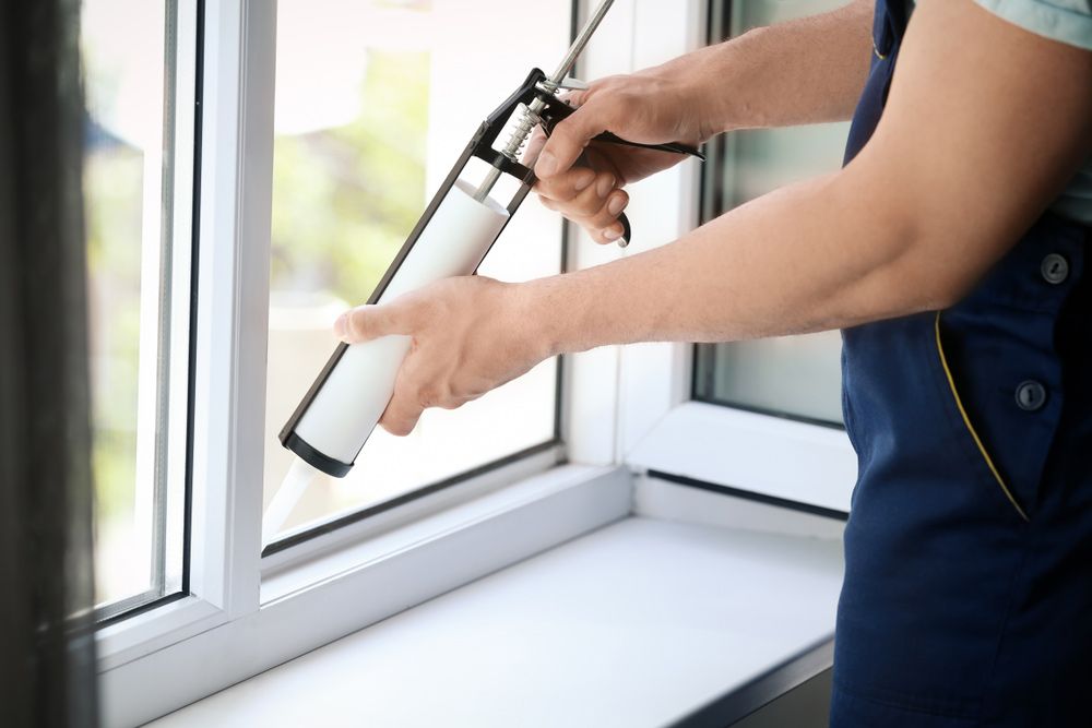 Construction Worker Sealing Window With Caulk Indoors — Emergency Glass Repairs & Replacement in Taminda, NSW