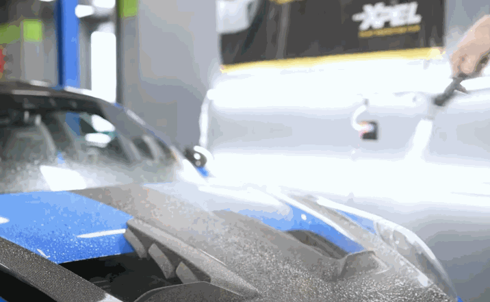 Detailer spraying water onto a sports car’s hood to prepare the surface for paint protection film installation.