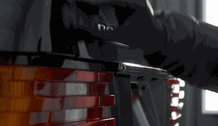 A gloved hand opens the rear hatch of a black car, showcasing the glossy finish and clean lines after ceramic coating application.