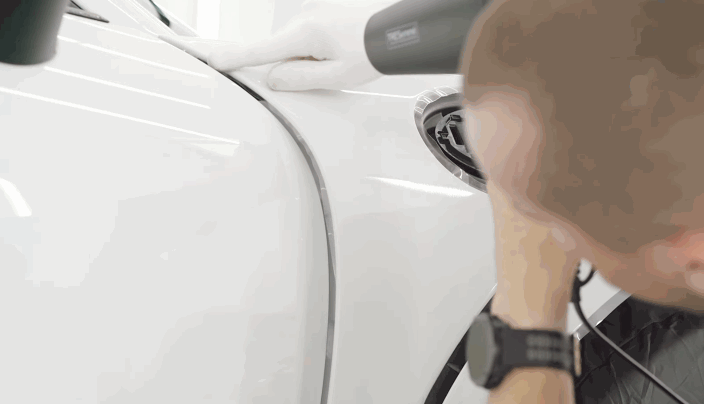 Installer using a heat gun to properly seal and contour paint protection film on a car’s fender.