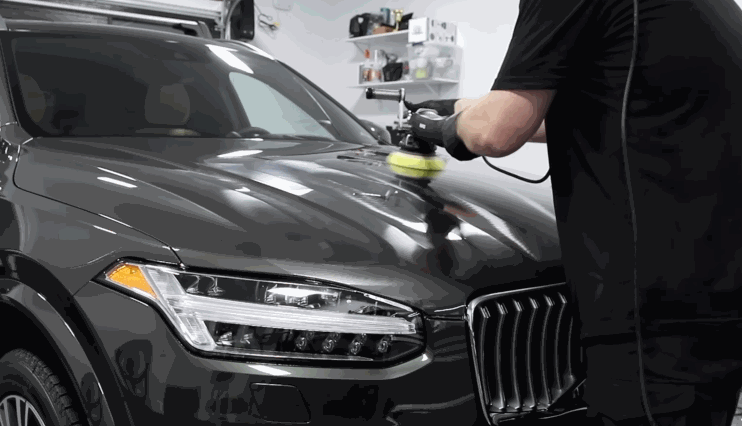 Detailer using a machine polisher to apply ceramic coating on a black SUV’s hood in a garage.
