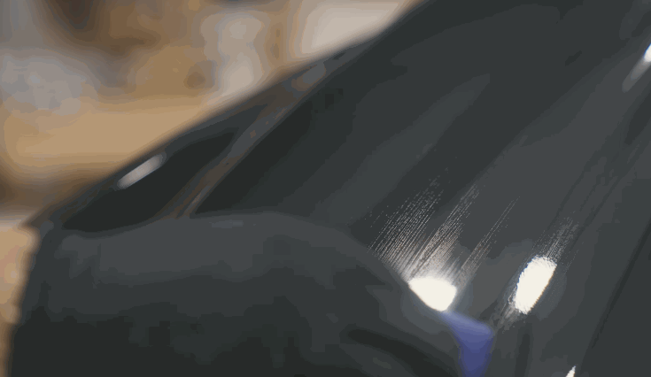 A gloved hand applies ceramic coating to a car’s glossy black surface using a microfiber applicator, leaving behind visible streaks.
