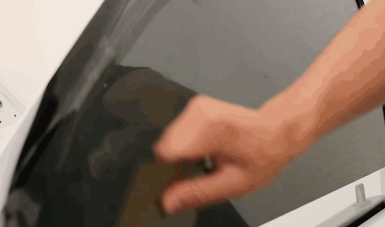 A technician smooths dark window tint onto a car side window by hand. The close up shows the film being pressed into place for even coverage.
