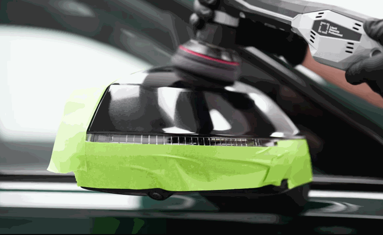 Technician polishes a black side mirror taped off with green masking tape during ceramic coating preparation.