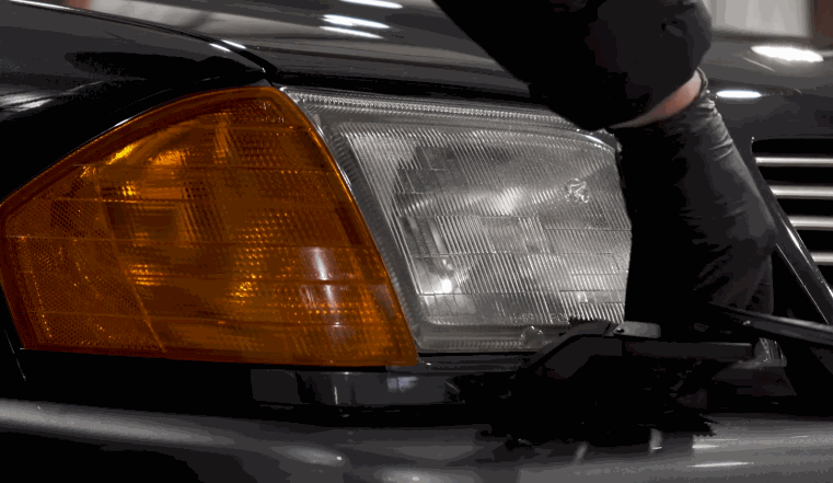 Detailer lifts the hood of a classic car with restored headlights and a protected finish using ceramic coating.