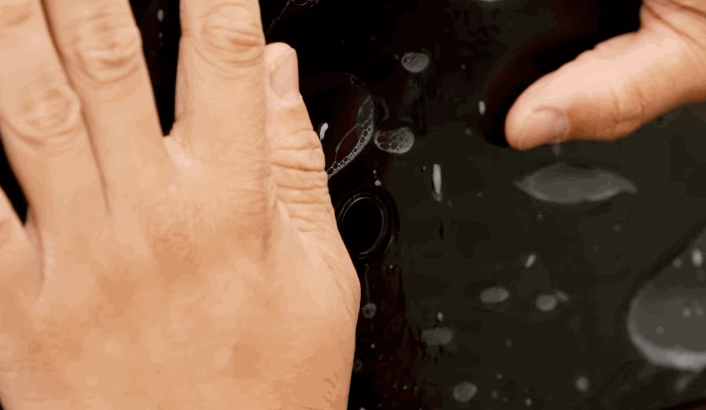 Hands pressing PPF onto a black car panel using a slip solution to position the film before final adhesion.