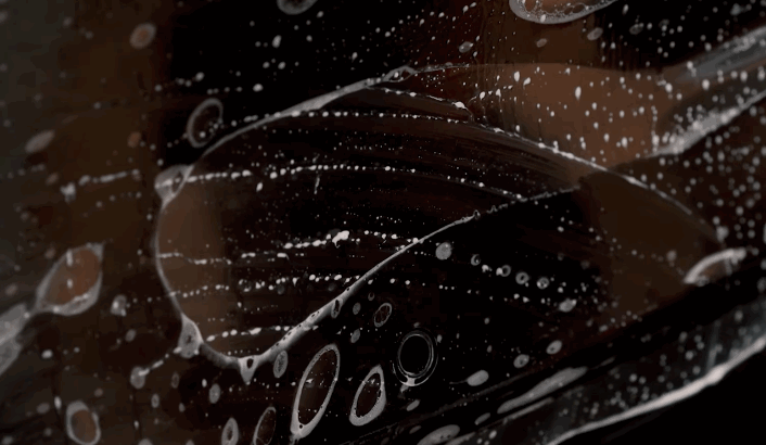 A detailed view of a glossy black car surface during paint protection film application, with soap and water bubbles highlighting the contour of the film.
