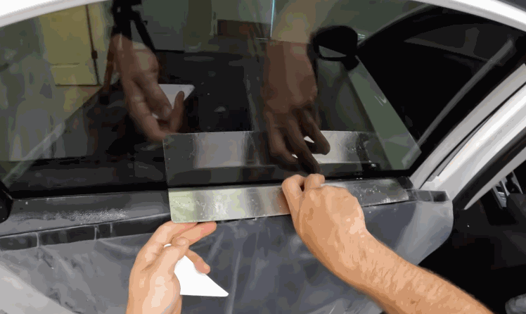 professional installing window tint film on car window using precision tools