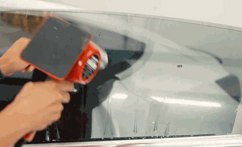 A technician uses a heat gun and squeegee during window tint installation on a Tesla side window. The film is being shaped against the glass for a clean fit.