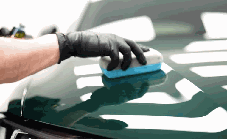 Gloved hand smooths a blue applicator across a glossy green hood during ceramic coating preparation.