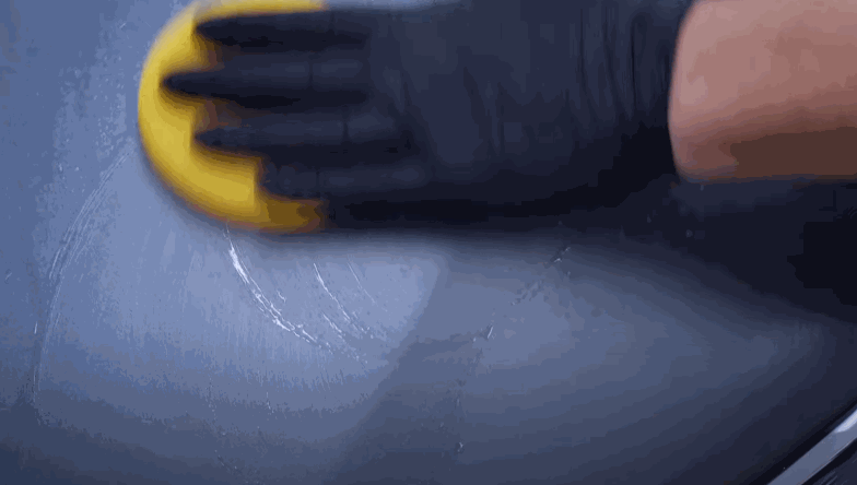 A person polishing the car's surface with a yellow sponge to ensure the even application of ceramic coating.