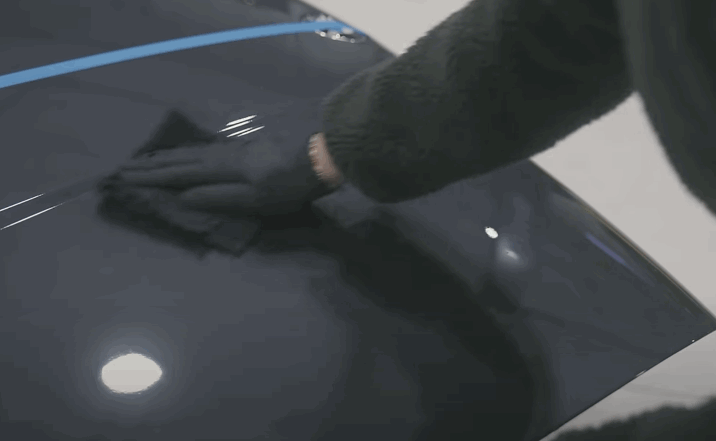 Detailer in gloves buffs a sectioned-off car hood with ceramic coating, highlighting contrast between treated and untreated paint.