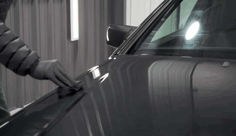 A hand gently wipes down a ceramic-coated car hood under studio lighting, revealing a flawless, reflective surface.