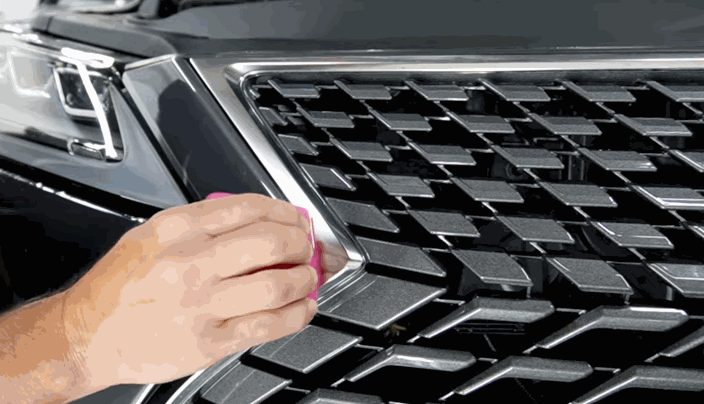 Close-up of a professional detailing the front grille of a car using a pink squeegee to apply paint protection film.