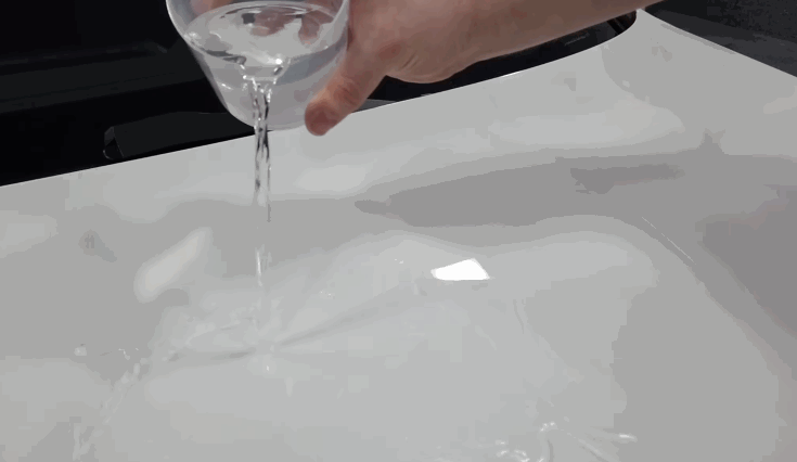 Water is poured onto a ceramic-coated car hood, showing how the coating repels liquid with a hydrophobic effect.
