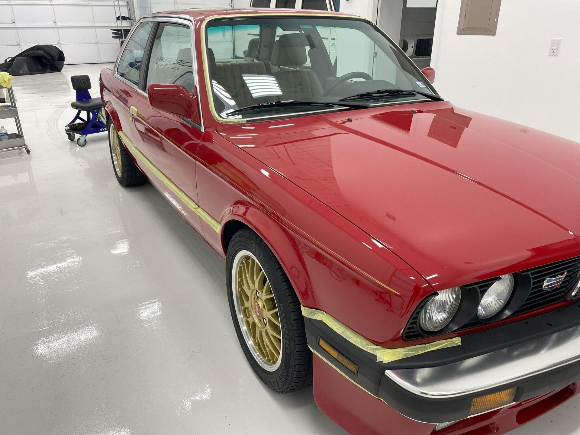 A red car with gold wheels is parked in a garage.