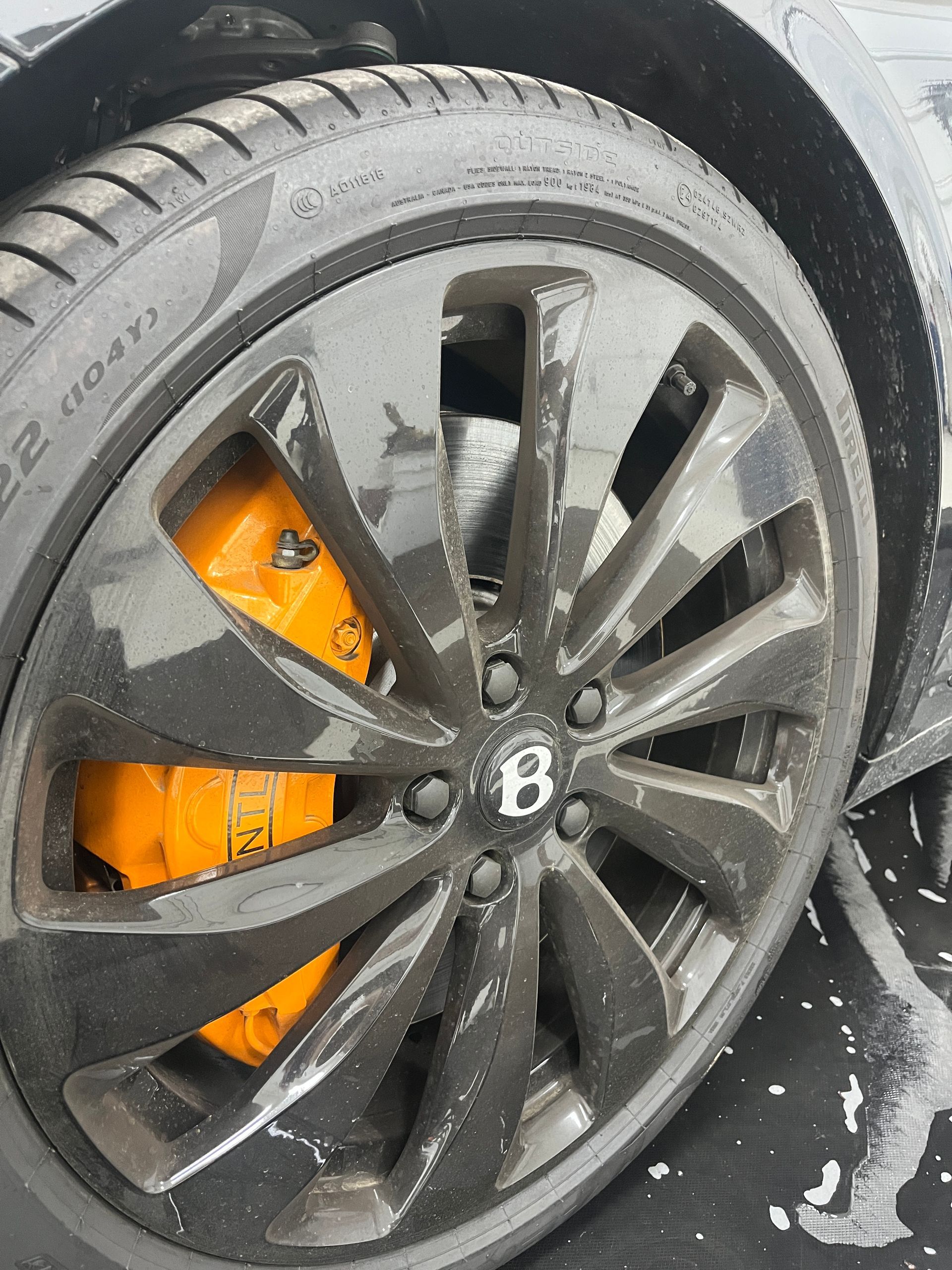 A 2025 Bentley Continental GT Black tire, black wheel face, and orange brake calipar  just arrived at Blue Ocean Auto Spa of Cedar Park Tx and is pictured here in our indoor wash bay and about to go through a deep cleaning