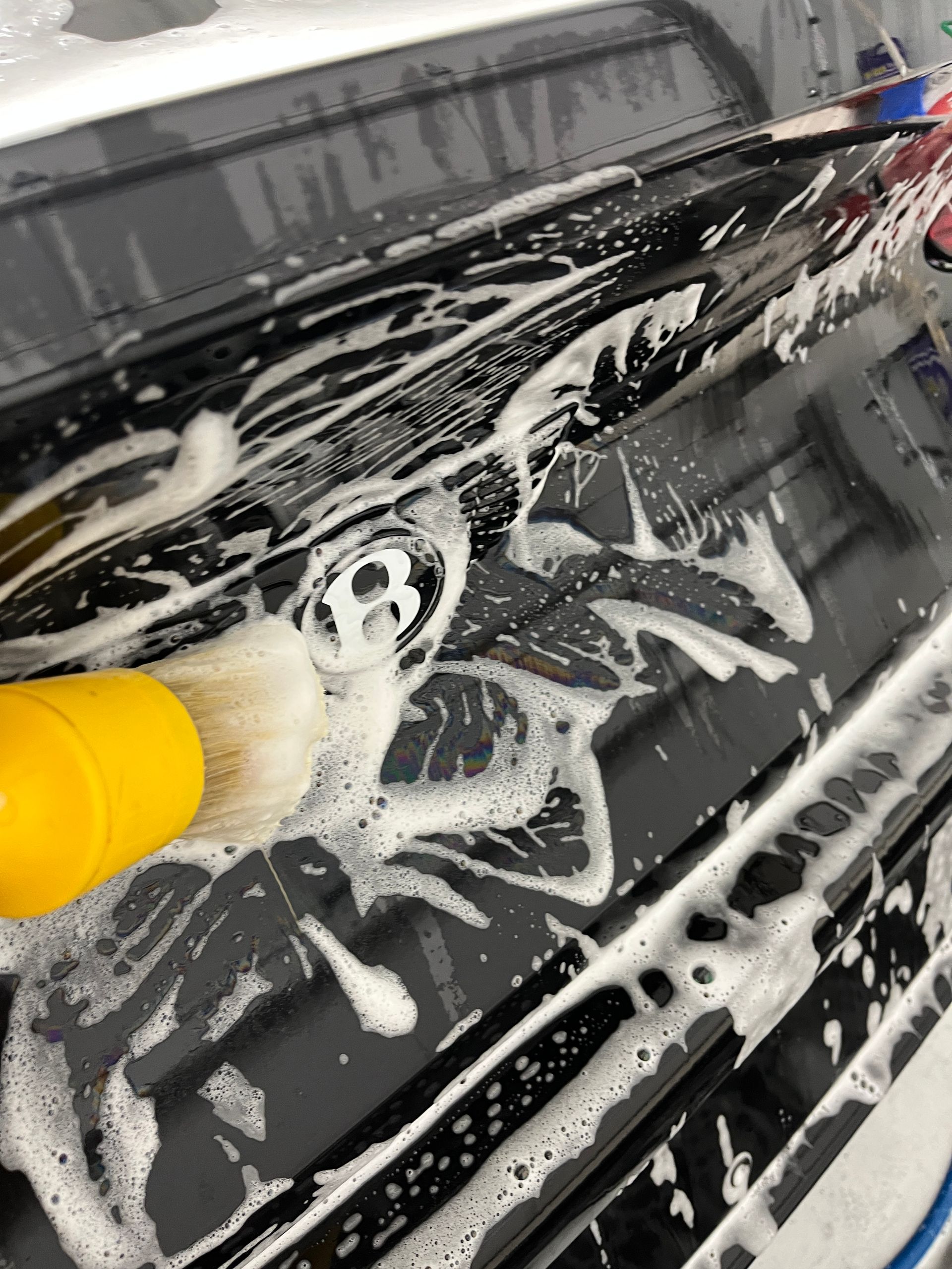 A detailing brush being used with gentle snow foam soap to remove dirt and grime around the Bentley emblem on the truck.