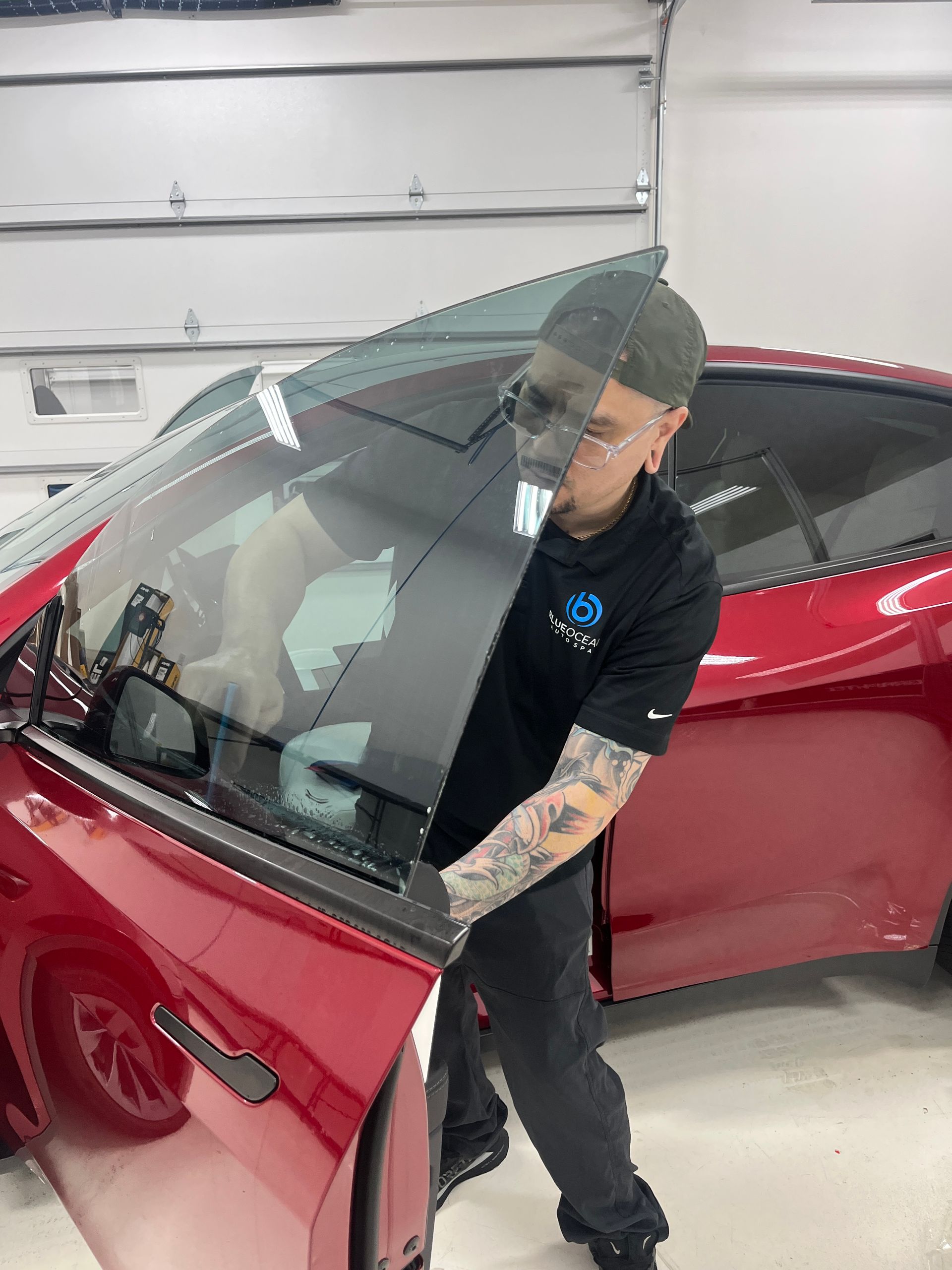 A window tint technician applies ceramic window tint to the front door window of a Tesla Model Y in a clean room at Blue Ocean Auto Spa of Cedar Park Tx