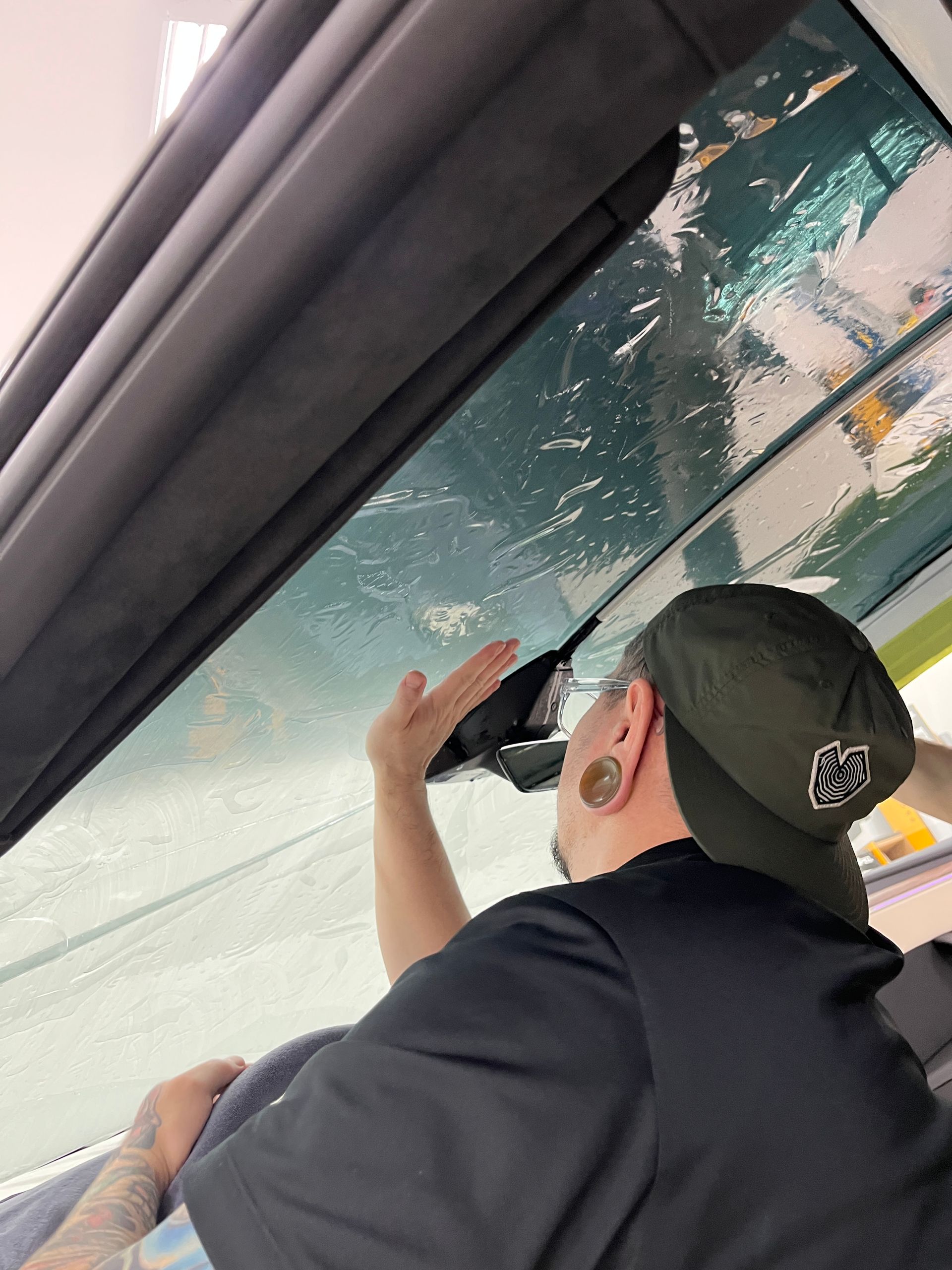 A technician hand positions film on a wet Tesla Model X windshield during a window tint installation. The close up shows the film and moisture along the glass before final smoothing.